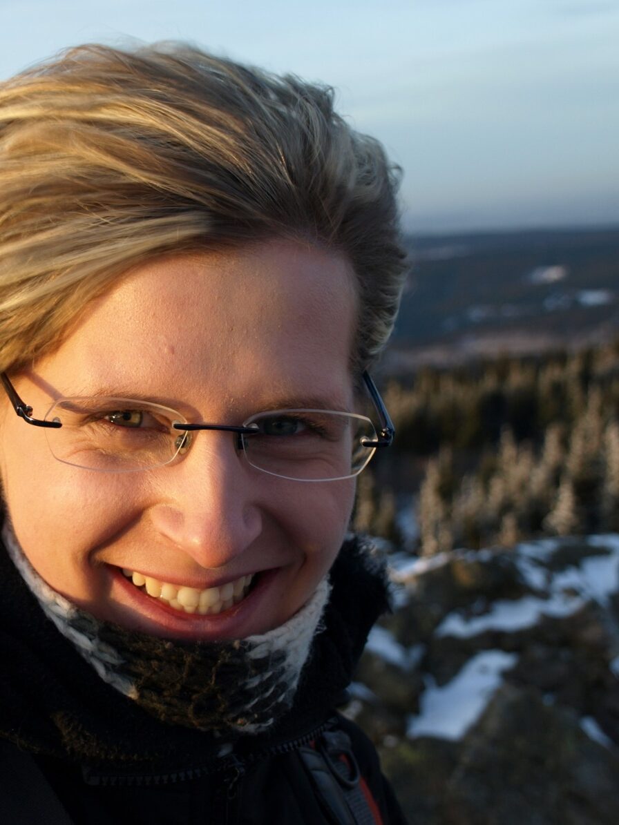 Person lächelt in die Kamera bei winterlicher Landschaft im Hintergrund.